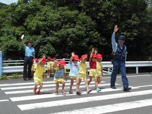 写真：手を挙げて横断歩道を渡る子供たちと警察官